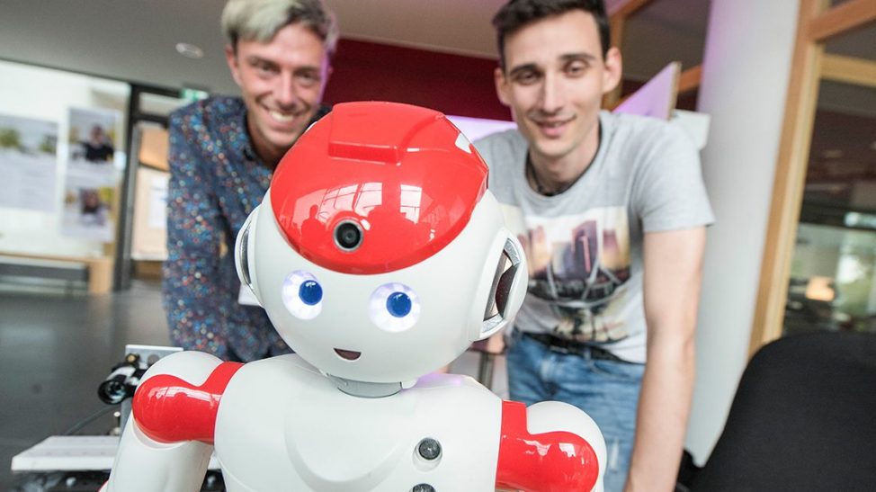 Little white Android with a red hat in front of two smiling men